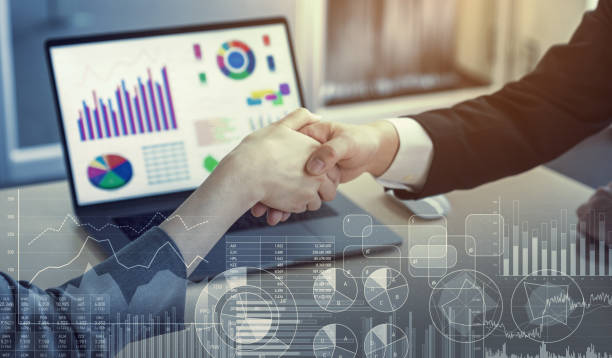 Business partners shaking hands over laptop charts.